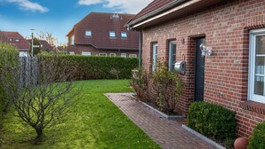 Un immeuble résidentiel à la façade en briques, doté d’un petit jardin avec une pelouse et des arbustes, et surplombant un ciel dégagé.