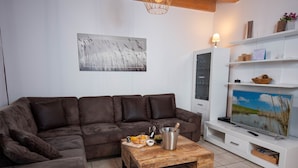 Un salon moderne avec un canapé en cuir marron, une table basse en bois sur laquelle repose une bouteille de champagne, et un téléviseur à écran plat posé sur un meuble blanc.