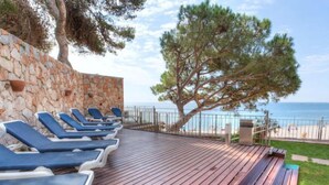 A wooden deck with lounge chairs and a stone wall.