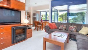 A modern living room with a flat-screen TV, wooden cabinets, a sofa, and a dining area with a table and chairs.
