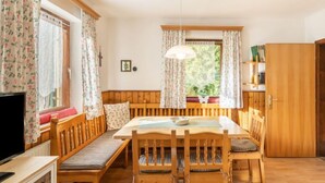 Ein gemütliches Zimmer mit einer hölzernen Bank und einem Tisch, einem Fernseher und einem fenster mit Vorhängen.