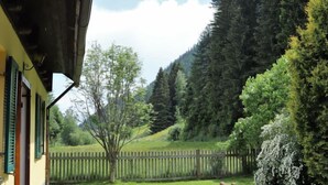 Eine hölzerne Bank und ein Picknicktisch vor einem Gebäude mit gelber Fassade und grünen Fensterläden.