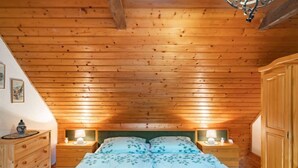 Ein gemütliches Schlafzimmer mit Holzbalkendecke, einem Bett mit floralem Bettzeug, Nachttischlampen und einer Kommode.
