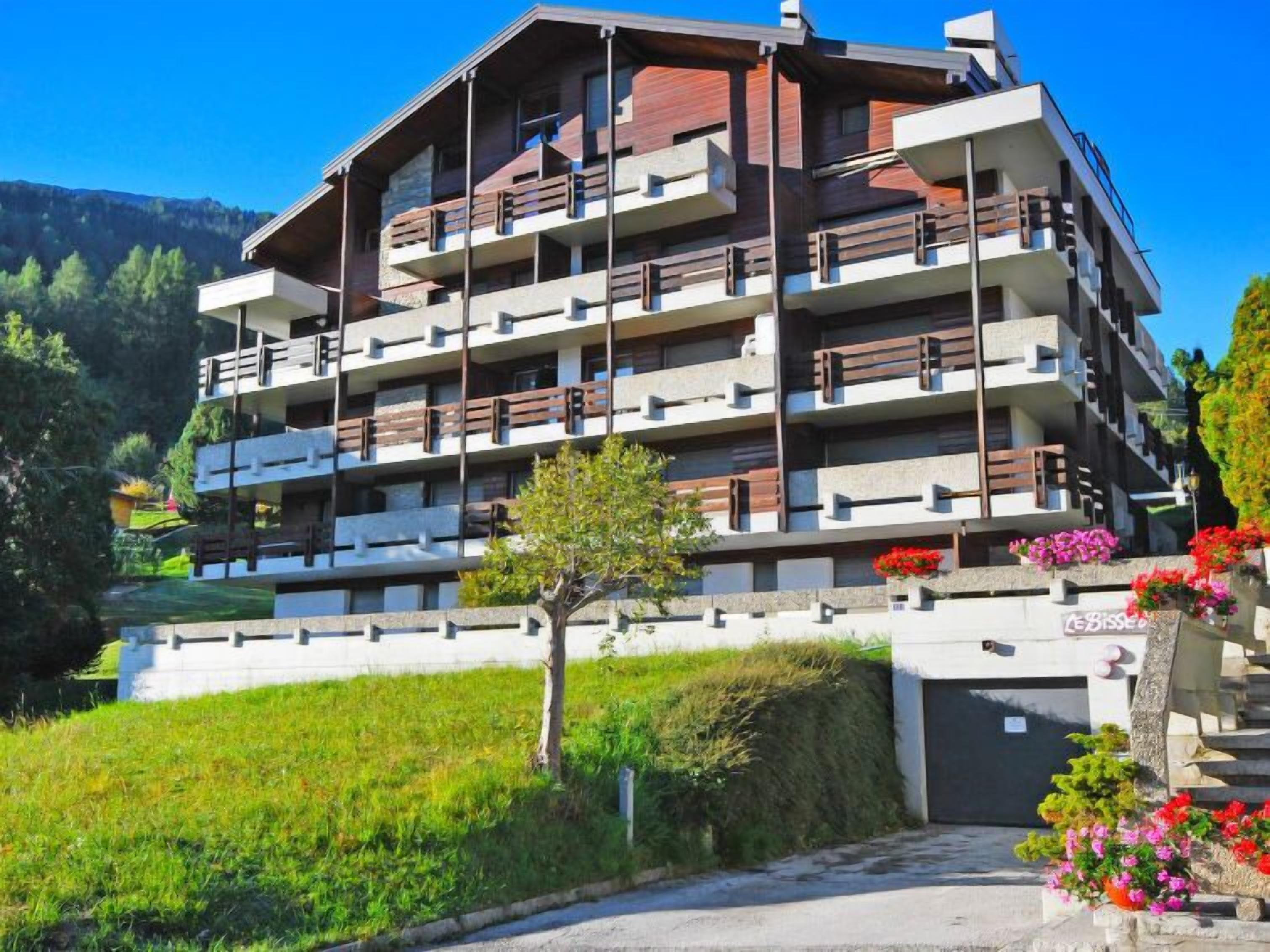 A multi-story hotel with balconies, a parking area, and a landscaped garden.