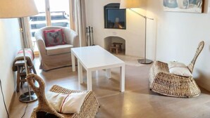 Una sala de estar con sofá, una mesa de centro, una silla de mimbre, una lámpara y un cuadro en la pared.