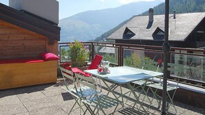 Un balcón con mesa y sillas, un rincón de estar con cojines y vistas a montañas.