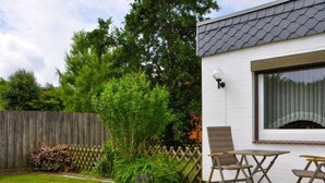 A patio with a table and chairs, surrounded by a garden with a wooden fence and various plants. - Rosengrund by Interhome (Büsum)