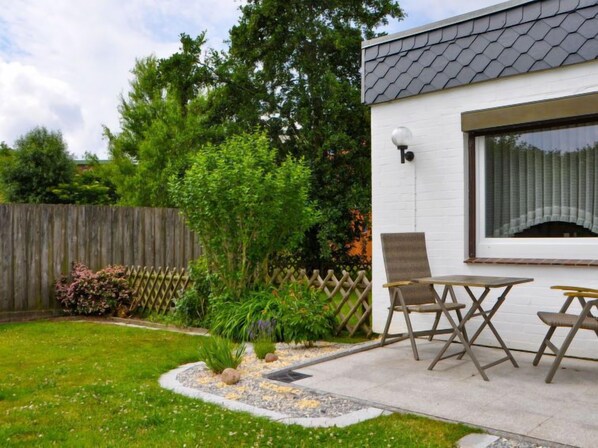 Une terrasse avec une table et des chaises, entourée d’un jardin agrémenté d’une clôture en bois et de diverses plantes.