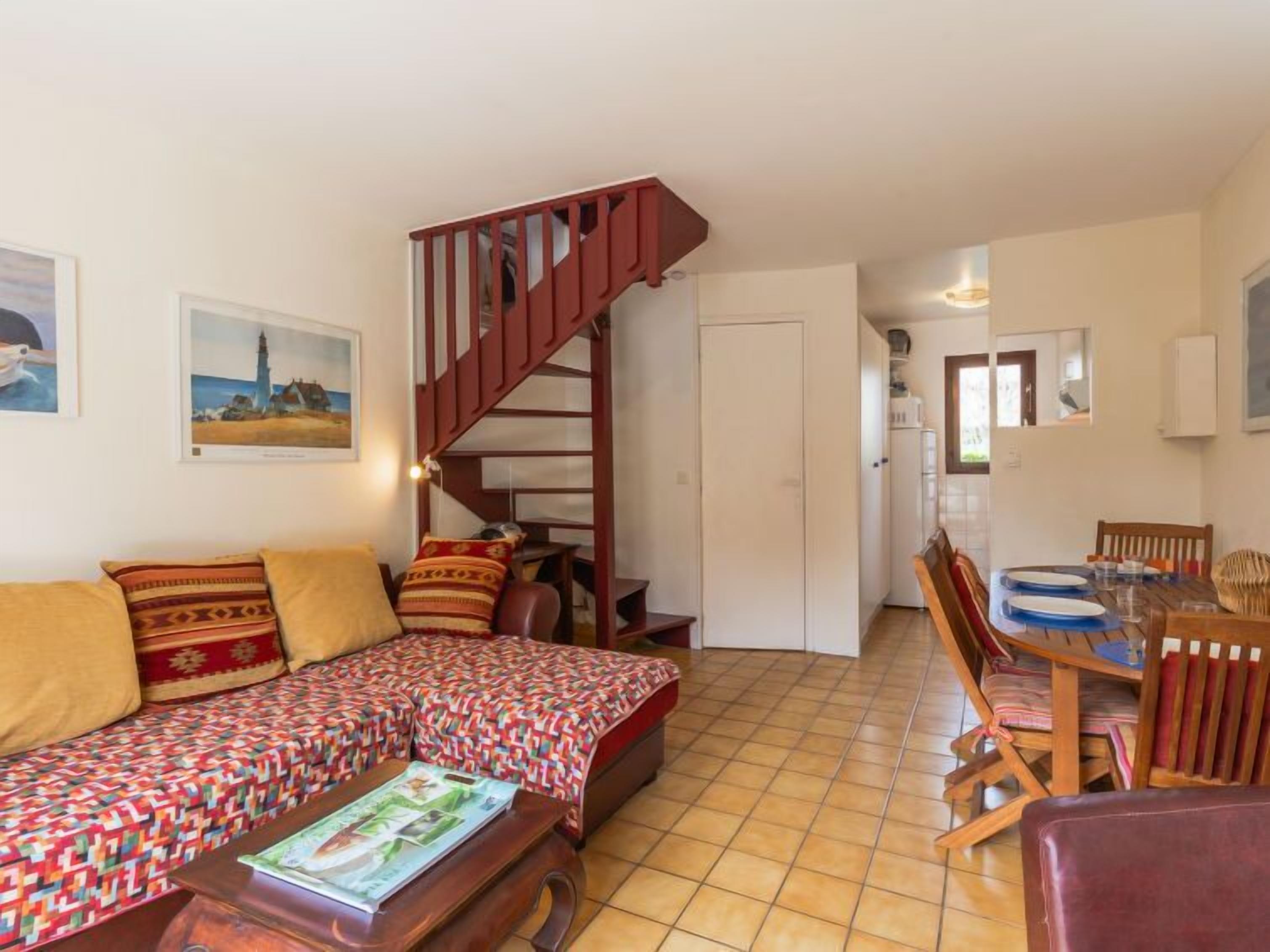 Un salon chaleureux avec un canapé, une table basse sur laquelle sont posés des magazines, un escalier en bois et un coin repas avec une table et des chaises.