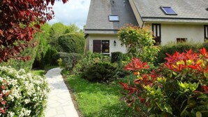 Ein Haus mit befestigtem Weg zum Eingang, umgeben von üppiger Vegetation und blühenden Pflanzen.