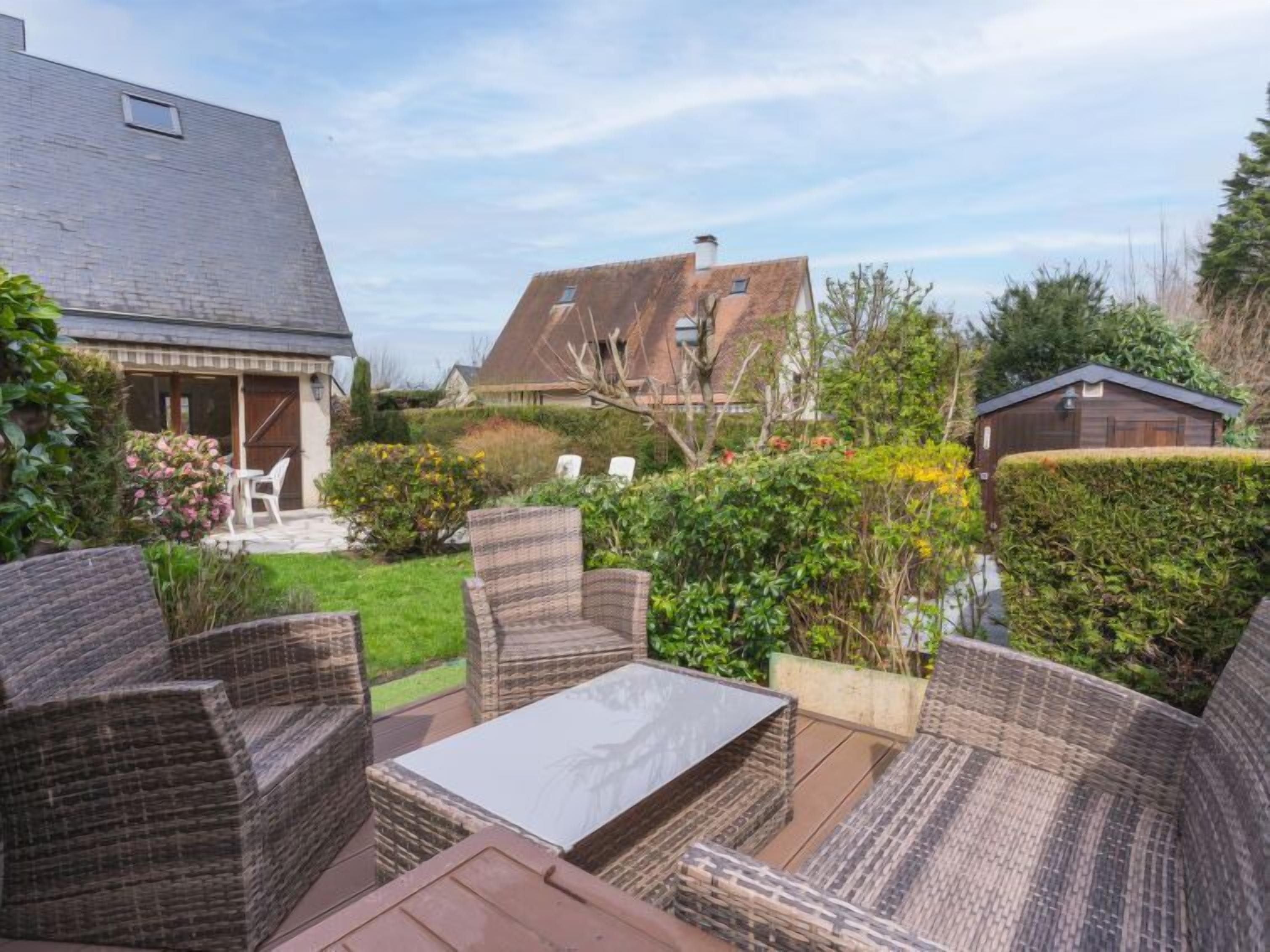 A patio area with wicker furniture and a table, surrounded by greenery and a view of neighboring houses.