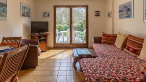 Ein Wohnzimmer mit einer Couch, einem Fernseher, einem Esstisch mit Stühlen und einer Schiebetür zu einem Außenbereich mit Tisch und Stühlen.