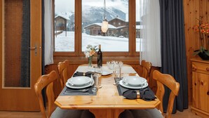 Ein Esszimmer mit Holztisch, gedeckt für vier Personen, einem Fenster mit Blick auf verschneite Häuser und einem Holzschrank auf der rechten Seite.