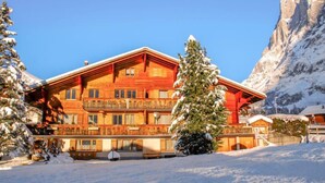 Eine große Holzhütte mit mehreren Balkonen, umgeben von schneebedeckten Bergen und Bäumen.