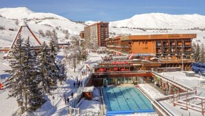 Um hotel com piscina, pistas de esqui e montanhas cobertas de neve ao fundo.