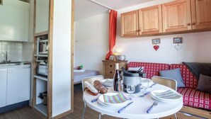 Cozinha compacta com armários brancos, mesa de jantar posta com pratos, talheres e chaleira.