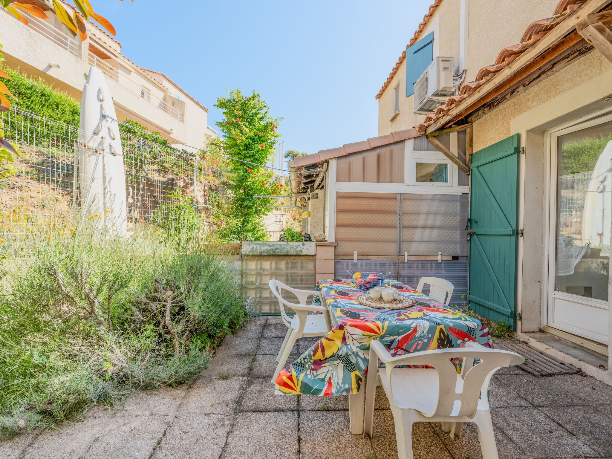 A patio with a table set for two, surrounded by greenery and a building with a tiled roof.