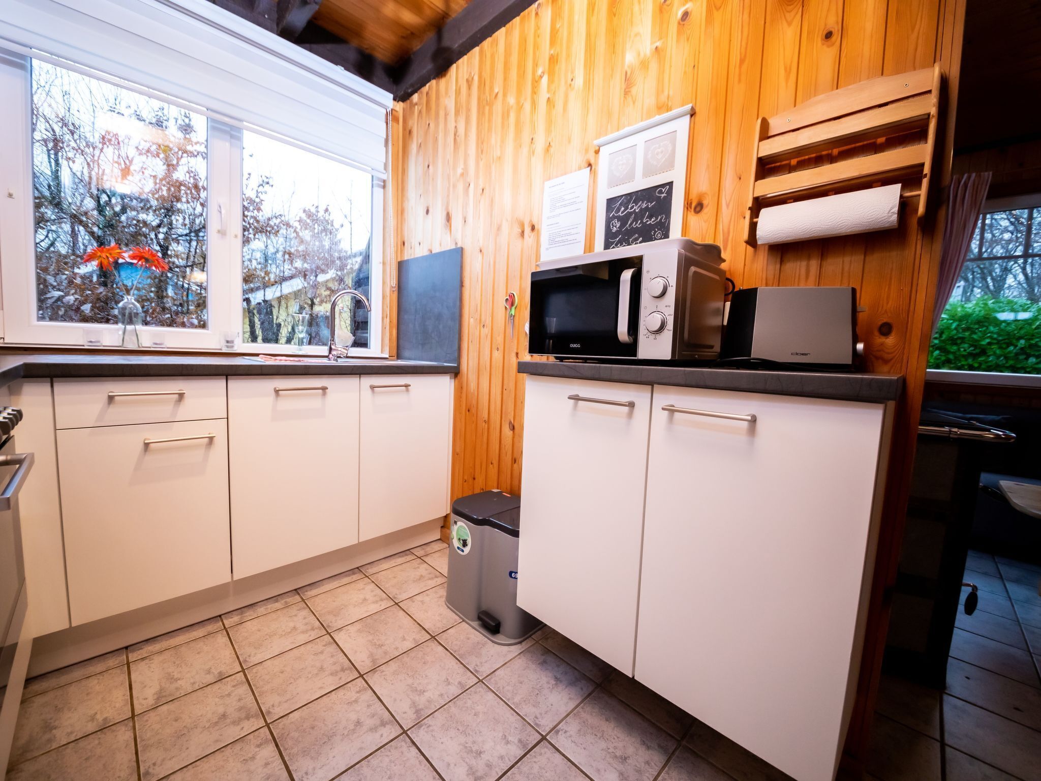 Une cuisine de taille réduite avec des murs en bois, un évier, un four à micro-ondes et une poubelle.
