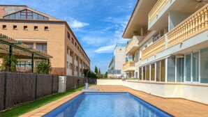 A swimming pool with a wooden deck, surrounded by buildings with balconies and large windows. - Residencial Roma by Interhome (Jávea)