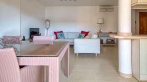A modern living room with a dining table and chairs, a sofa with colorful cushions, and a kitchen area with a counter and cabinets. - Residencial Roma by Interhome (Jávea)