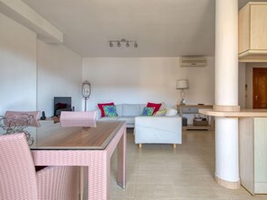 A modern living room with a dining table and chairs, a sofa with colorful cushions, and a kitchen area with a counter and cabinets.