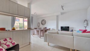 A modern living room with a white sofa, a dining area with a table and chairs, and a kitchen with light wood cabinets. - Residencial Roma by Interhome (Jávea)