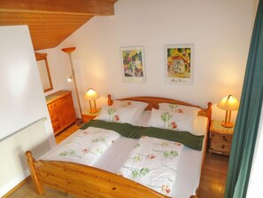A cozy bedroom with a wooden bed, two bedside lamps, a dresser, and two wall art pieces. - Fischer by Interhome (Lechbruck am See)