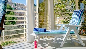 A sunlit outdoor seating area with a lounge chair and a rolled towel, a water bottle, and a view of a cityscape. - Apartment Zeus by Interhome (Calpe/Calp)