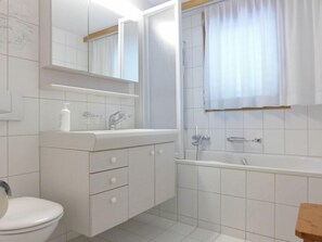 A modern bathroom with a toilet, sink, mirror, and bathtub. - Rose Apt. Y by Interhome (Wengen)