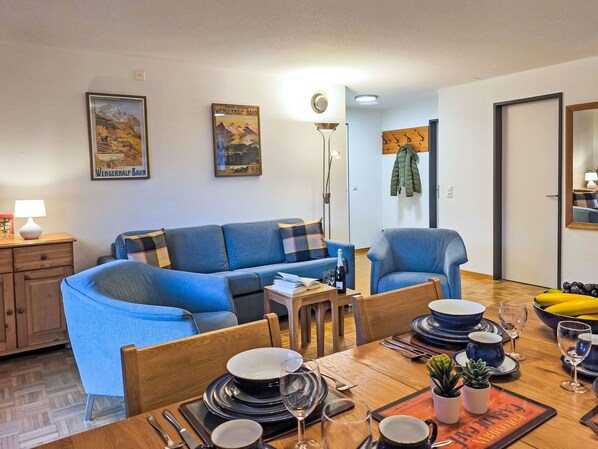 A living room with a sofa, a dining table set with plates, glasses, and a bottle, and a lamp on a side table.