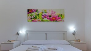 Een net opgemaakt bed met opgevouwen witte handdoeken, een wit hoofdeinde en twee nachtkastjes met lampen en boeken.