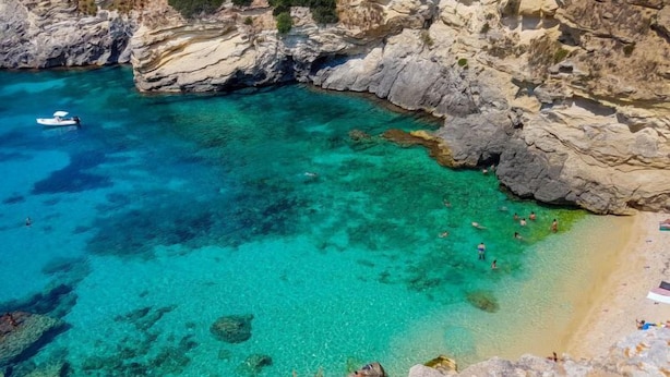Een kuststrand met helder turquoise water, rotsachtige kliffen en een klein bootje afgemeerd dichtbij de kust.
