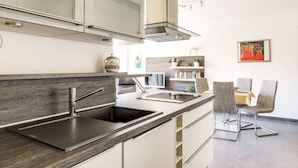 Une cuisine moderne avec un plan de travail en bois foncé, un évier en acier inoxydable et des meubles blancs. On aperçoit à l’arrière un coin repas avec une table et des chaises.