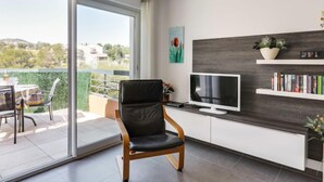 Un salon moderne doté d’une porte-fenêtre coulissante donnant sur un balcon, d’un téléviseur à écran plat, d’une bibliothèque et d’un fauteuil en cuir confortable.