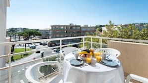 A balcony with a table set for breakfast, overlooking a street with cars and buildings. - Les Hesperides by Interhome (Cavalaire)