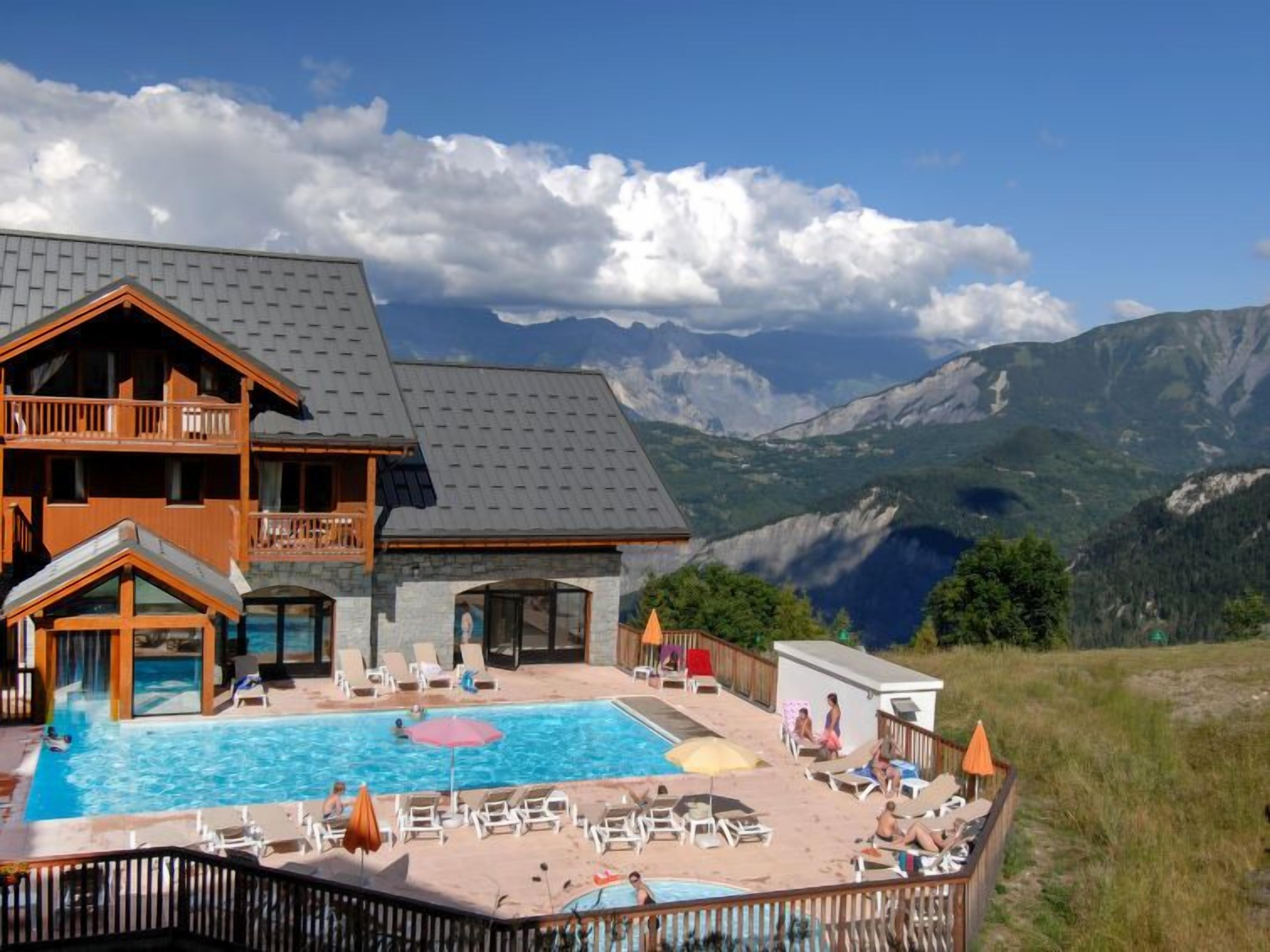 A hotel with a pool, lounge chairs, and mountain views.