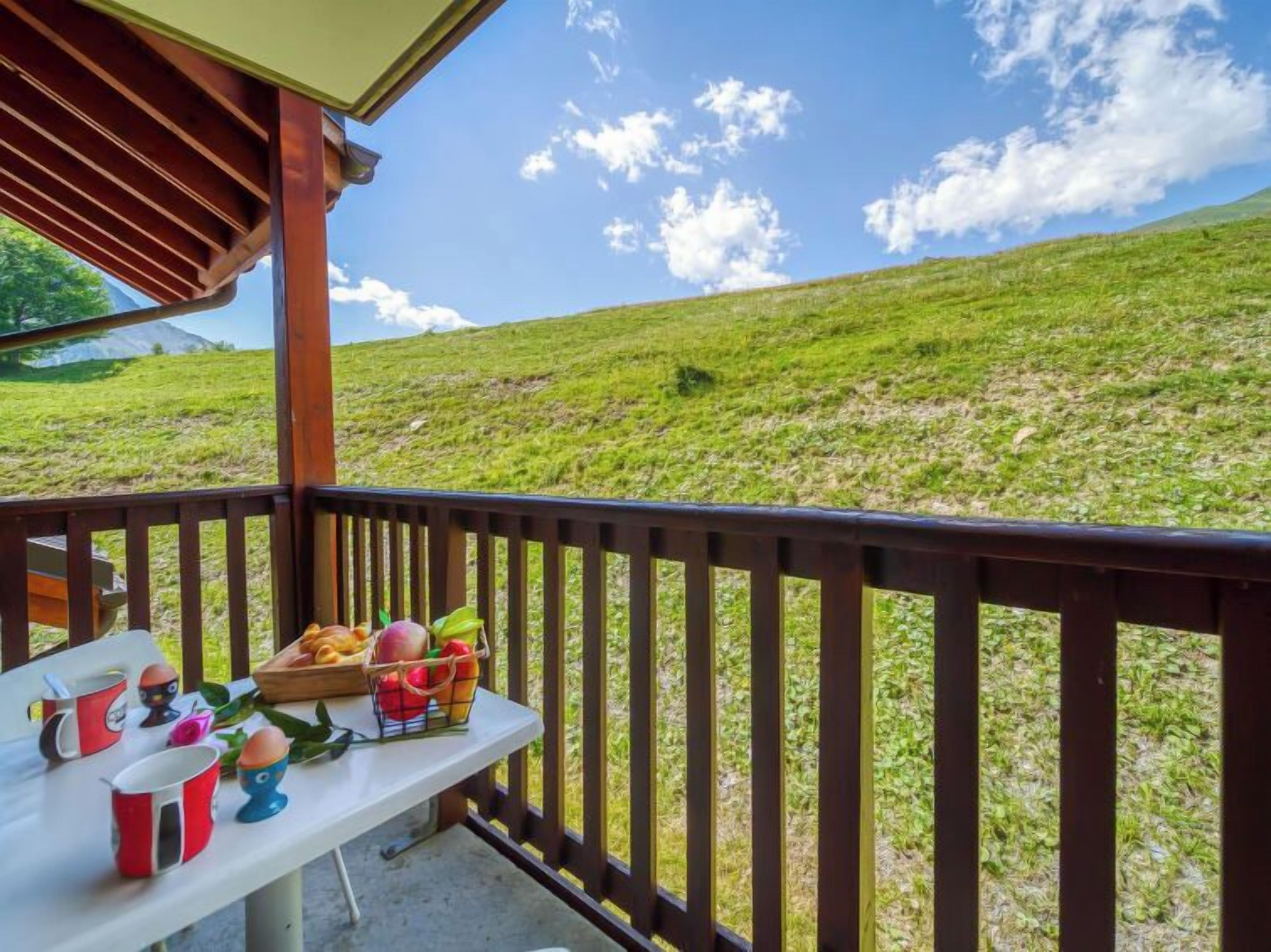 Ein Balkon mit Frühstückstisch, mit Blick auf einen grünen Hang.