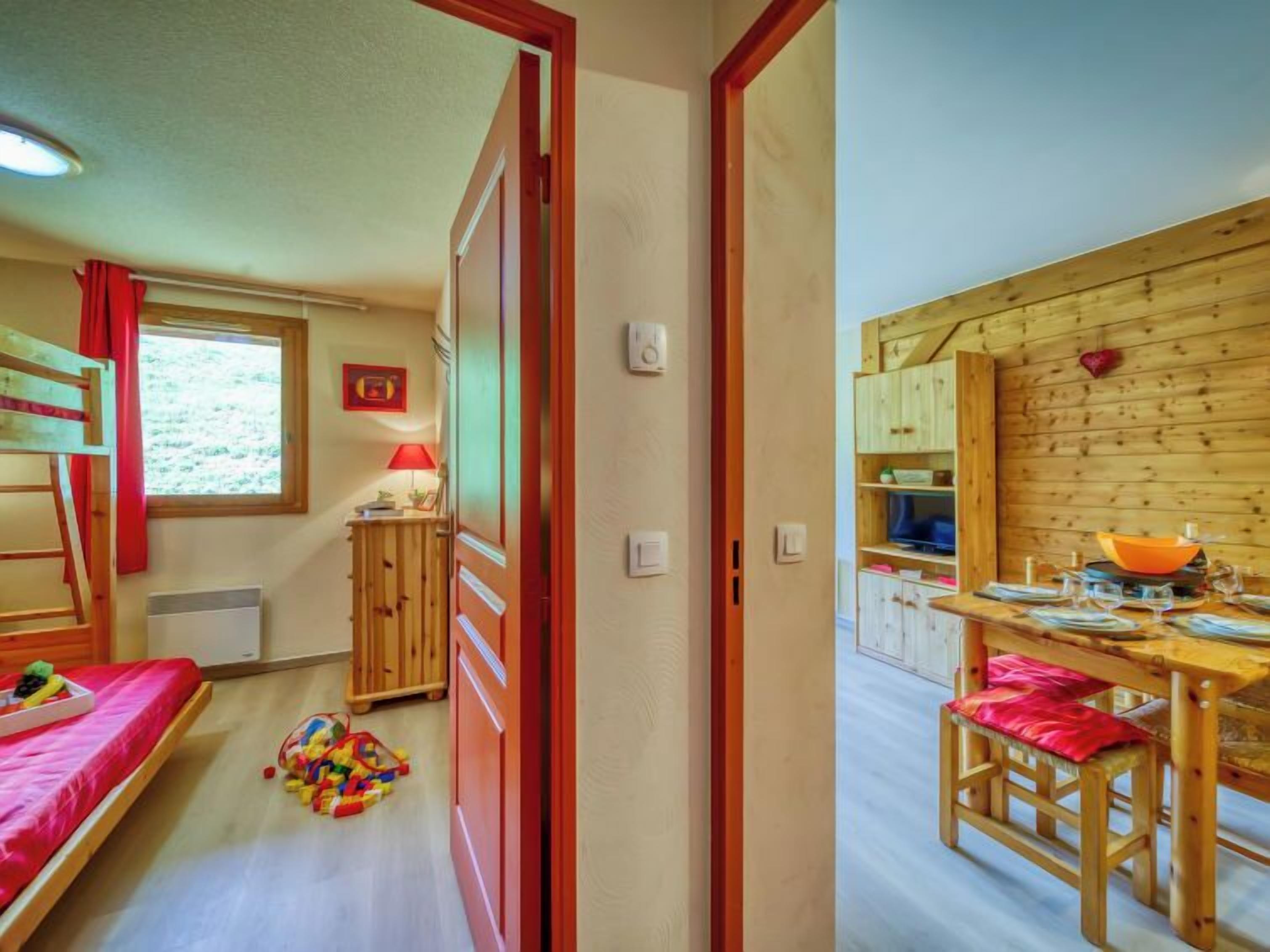 Una habitación con literas, una mesita con lámpara y una kitchenette que incluye televisión y armarios de madera.