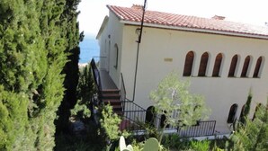 A building with a red-tiled roof, a staircase leading to a door, and a view of the sea. - Apartment Cathy by Interhome (Llançà)