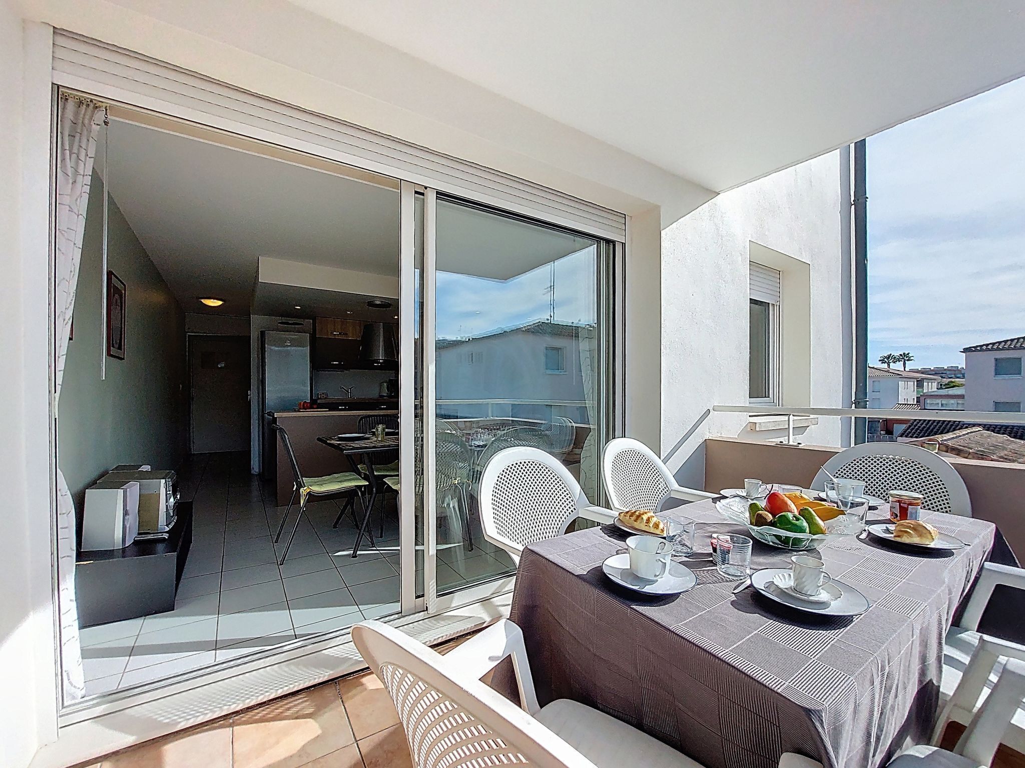 Un balcone con un tavolo da pranzo per due persone, una porta scorrevole in vetro che dà su una cucina e vista su edifici in lontananza.