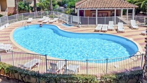 En swimmingpool med solstolar och en liten byggnad med ett tak täckt av tegelpannor.