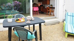 Un comedor con una mesa preparada para dos personas, una planta en maceta y una cesta de fruta.