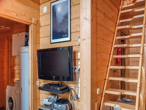 A wooden interior with a mounted TV, a washing machine, and a ladder.