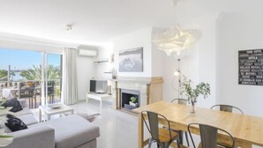 A modern living room with a fireplace, a dining table, and a sofa. There is a TV on a stand and a large window overlooking a body of water. - Nautic 3 by Interhome (Port d'Alcúdia)