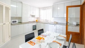 A modern kitchen with white cabinets, a microwave, and a dining area set up with a table, chairs, and a vase of flowers. - Nautic 3 by Interhome (Port d'Alcúdia)