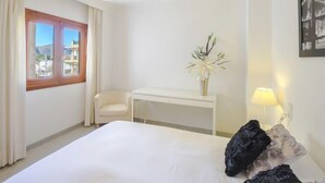 A hotel room with a bed, a desk, a chair, a vase with flowers, and a lamp. - Nautic 3 by Interhome (Port d'Alcúdia)