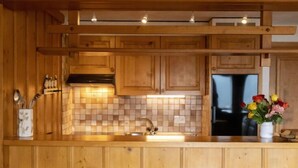 Una cucina in legno con rivestimento a piastrelle, un lavello in acciaio inossidabile e un frigorifero. Ci sono tre sgabelli di legno al bancone.