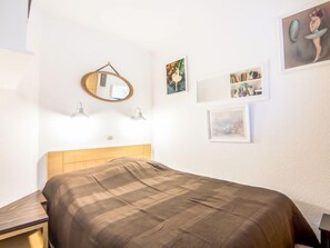 Ein Schlafzimmer mit einem Bett, einem Holz-Kopfteil, einem runden Spiegel und Wandleuchten.