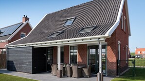 Una casa moderna con techo inclinado, paneles solares y un porche cubierto con mobiliario exterior.