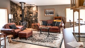 Una sala de estar acogedora con pared de piedra, muebles de cuero, chimenea y ventilador de techo.